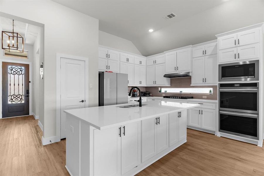 Kitchen featuring stainless steel appliances, a sink, vaulted ceiling, white cabinets, and recessed lighting Kitchen featuring stainless steel appliances, a sink, vaulted ceiling, white cabinets, and recessed lighting