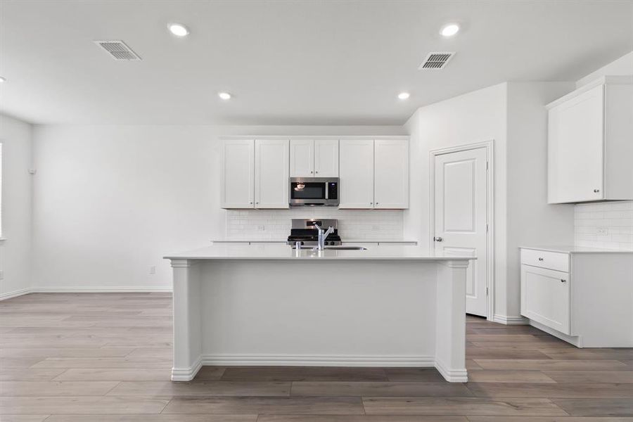 Kitchen with white cabinets, backsplash, stainless steel appliances, a center island with sink, and light hardwood / wood-style floors