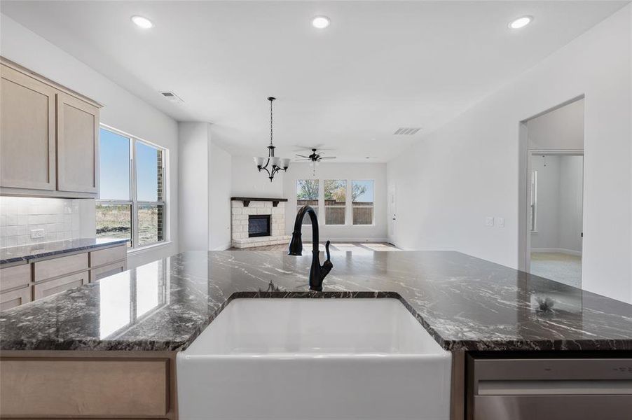 Kitchen with dark stone counters, recessed lighting, stainless steel dishwasher, open floor plan, and a stone fireplace