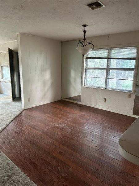 Unfurnished dining area featuring wood walls, a textured ceiling, and dark wood-style floors