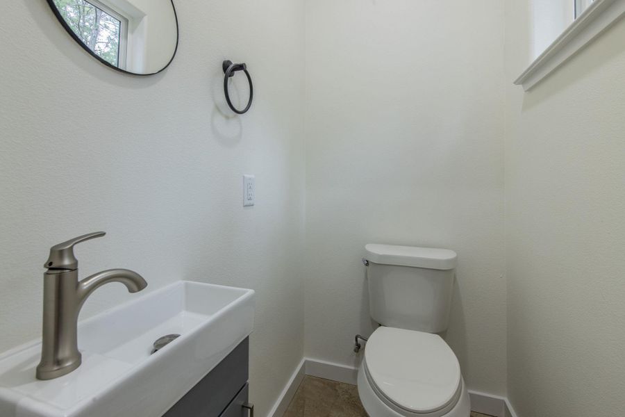 Compact powder room featuring a wall-mounted rectangular vessel sink with a brushed nickel faucet, a round black-framed mirror, and a modern toilet Compact powder room featuring a wall-mounted rectangular vessel sink with a brushed nickel faucet, a round black-framed mirror, and a modern toilet