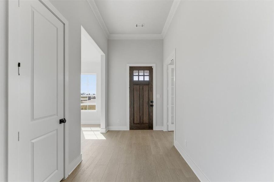 Foyer entrance featuring light wood-type flooring and ornamental molding Foyer entrance featuring light wood-type flooring and ornamental molding