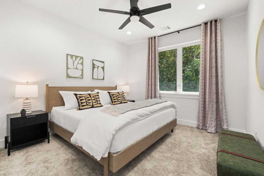 This cozy bedroom features a modern ceiling fan, and ample natural light from a large window. The space is accented with soft neutral carpeting for a warm, inviting feel.