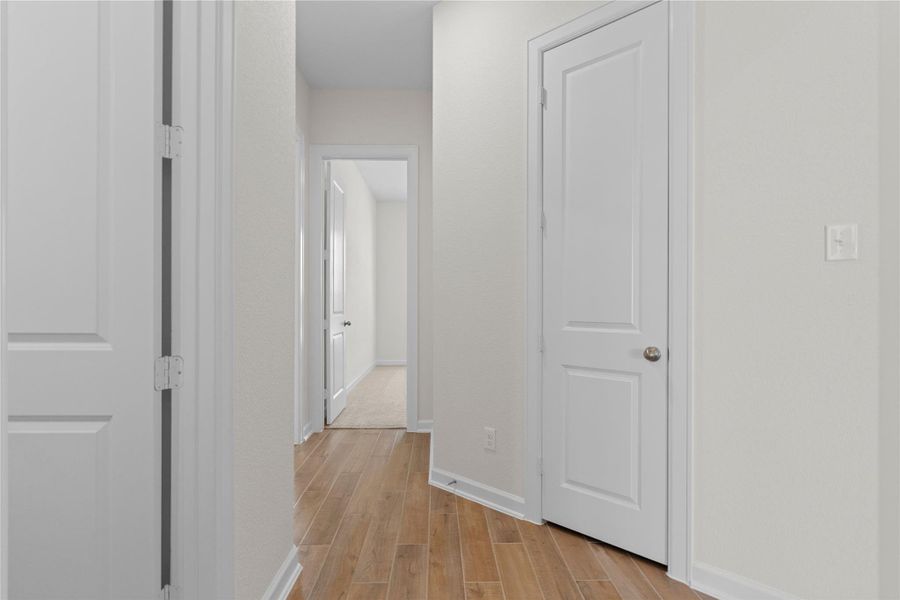 The hallway view showcases the transition from plush carpeted bedrooms to elegant wood like tile flooring in the main living areas, highlighting the thoughtful layout and flow of the home, with clean lines and quality finishes that enhance everyday living.