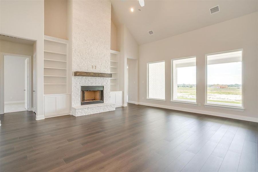 Unfurnished living room with high vaulted ceiling, a fireplace, built in shelves, and dark hardwood / wood-style flooring