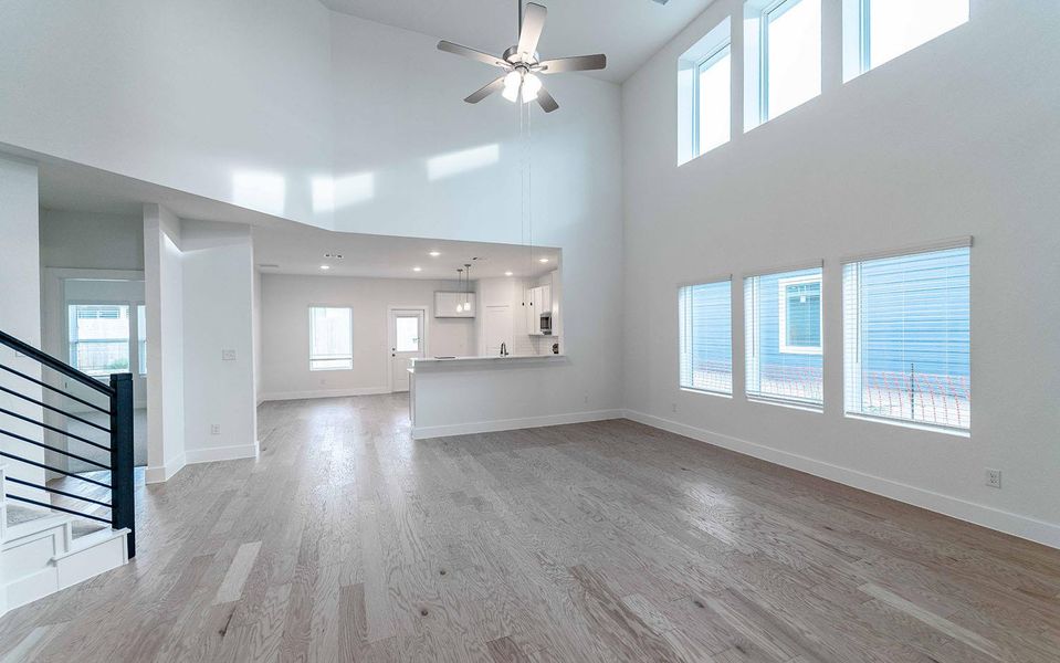 Unfurnished living room featuring light wood finished floors, a ceiling fan, and a high ceiling Unfurnished living room featuring light wood finished floors, a ceiling fan, and a high ceiling