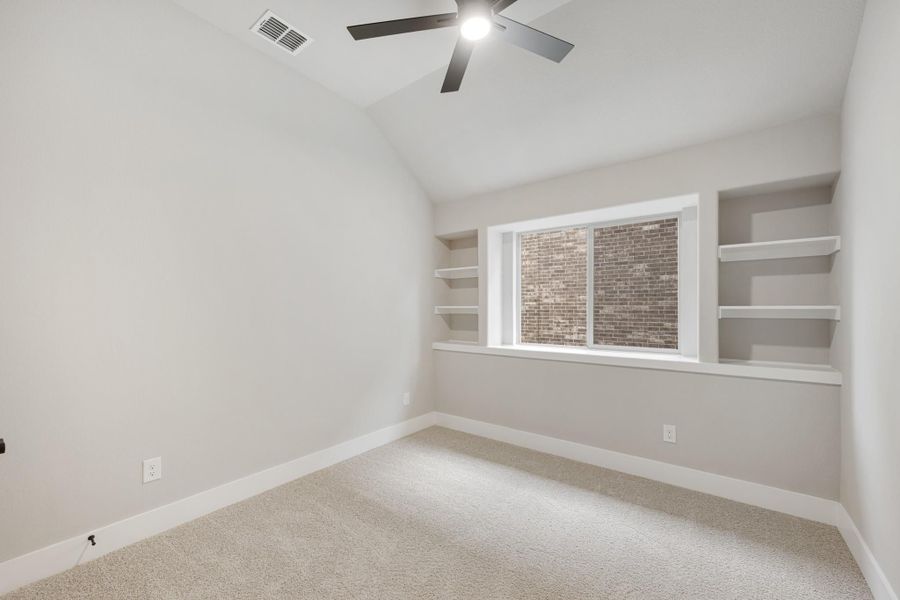 Empty bedroom with vaulted ceiling, ceiling fan, built-in shelves, and carpet flooring