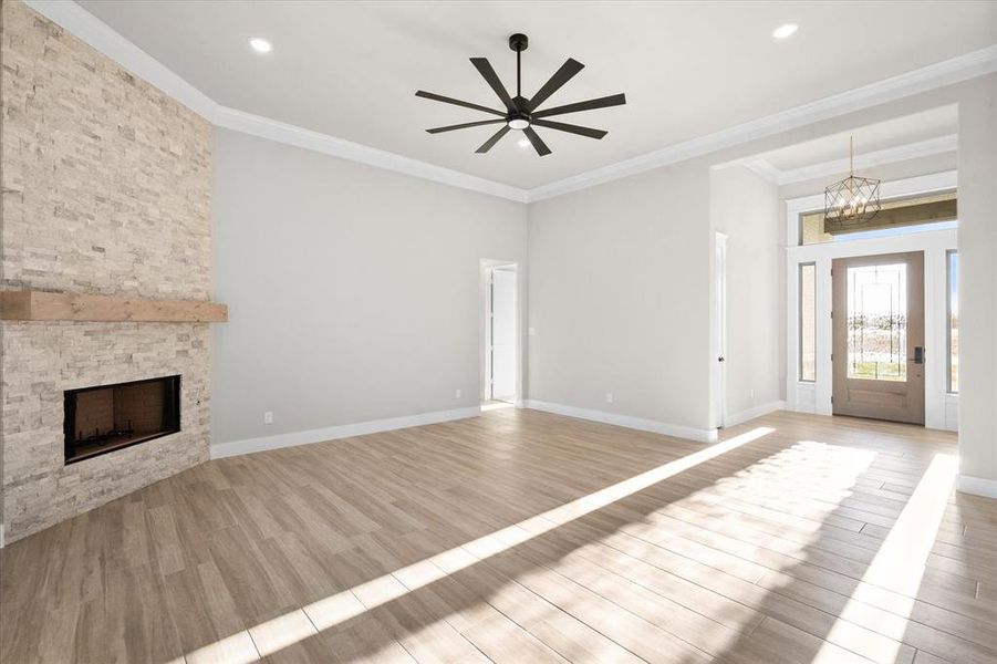 Unfurnished living room with a fireplace, light wood-type flooring, ceiling fan with notable chandelier, and crown molding