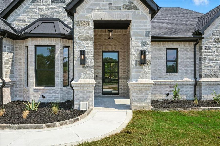 Property entrance featuring brick siding, a yard, stone siding, and roof with shingles