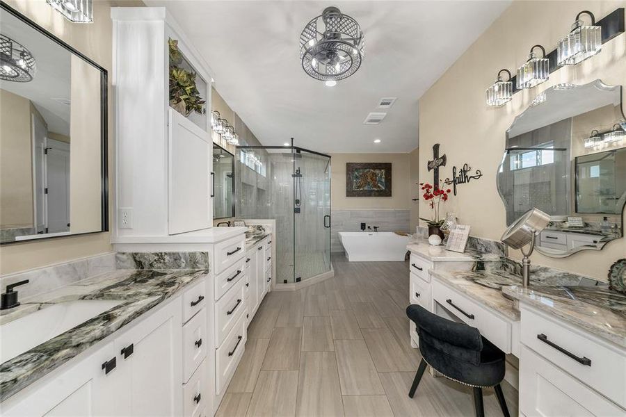 Bathroom with two vanities, a stall shower, a freestanding tub, wainscoting, and recessed lighting