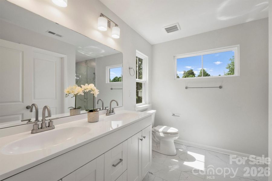 Primary ensuite bathroom with double vanity and tile floors.