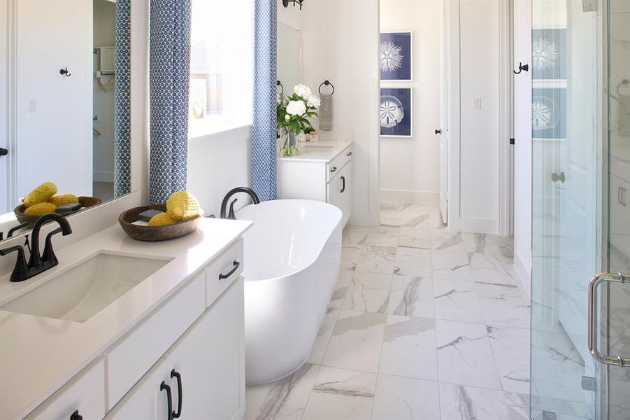 Full bath featuring two vanities, light marble finish flooring, a freestanding tub, and a shower stall