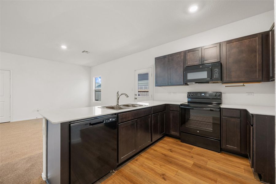 Kitchen with black appliances, a peninsula, dark brown cabinetry, light countertops, and recessed lighting Kitchen with black appliances, a peninsula, dark brown cabinetry, light countertops, and recessed lighting