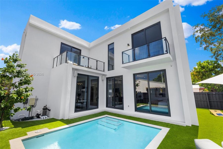 Modern two-story exterior featuring white stucco finish, dual glass-railed balconies, expansive sliding glass doors, and a private swimming pool with integrated stairs