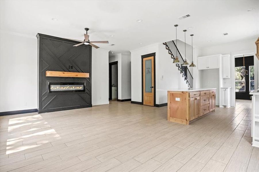 Kitchen with a large fireplace, open floor plan, a kitchen island, crown molding, and light brown cabinets