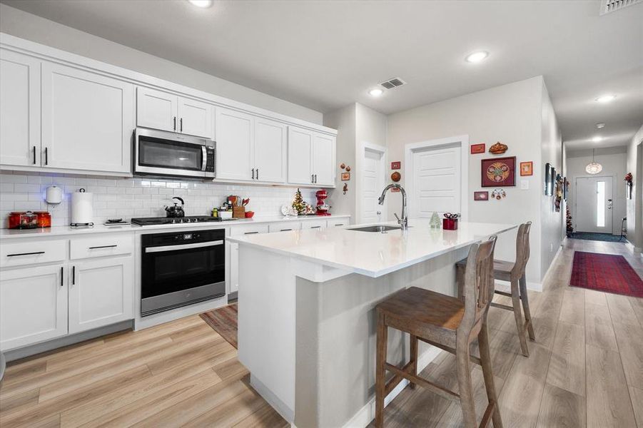 Kitchen featuring appliances with stainless steel finishes, light wood finished floors, white cabinetry, a breakfast bar area, and recessed lighting Kitchen featuring appliances with stainless steel finishes, light wood finished floors, white cabinetry, a breakfast bar area, and recessed lighting