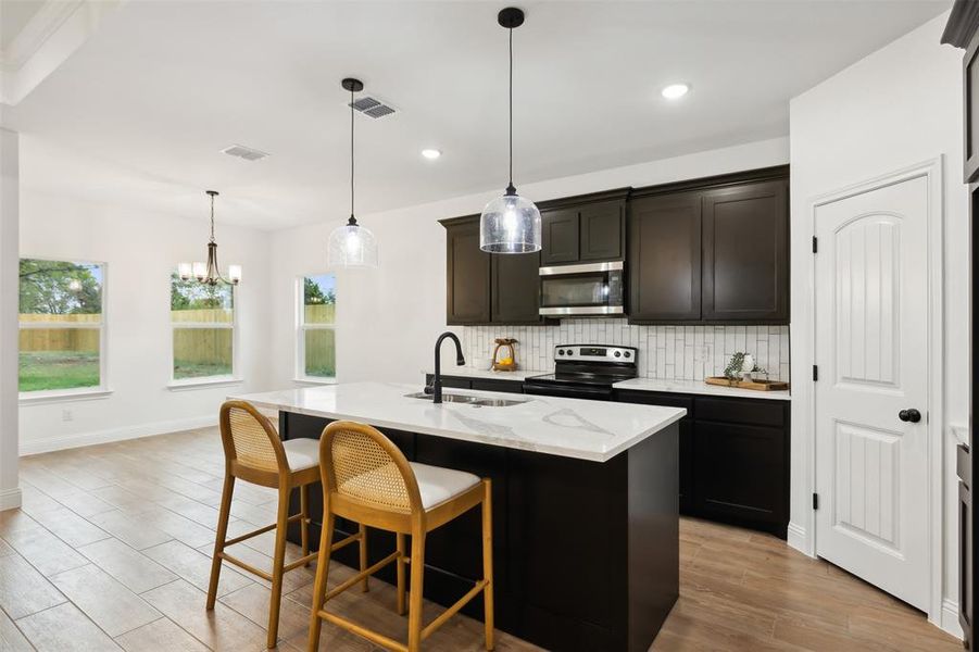 Kitchen with stainless steel appliances, backsplash, hanging light fixtures, sink, and a kitchen island with sink