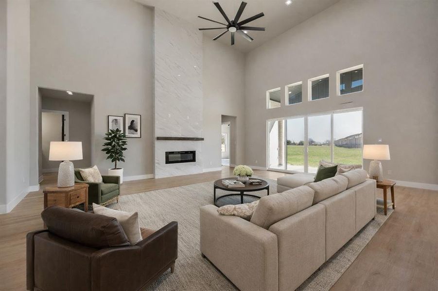 Living room with light wood finished floors, a ceiling fan, a fireplace, a high ceiling, and recessed lighting