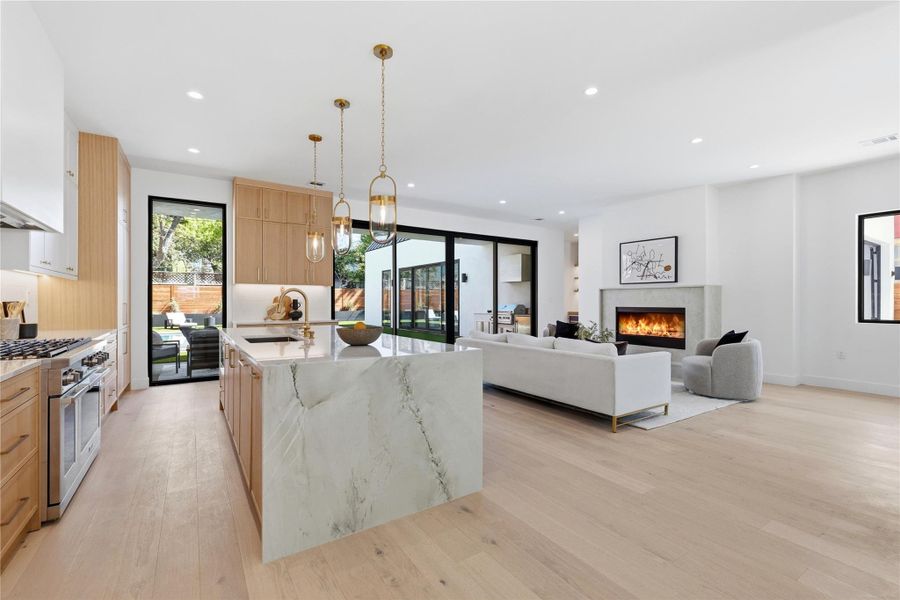 Dual tone kitchen featuring a center island with sink, light stone countertops, a premium fireplace, range with two ovens, and two tone color scheme