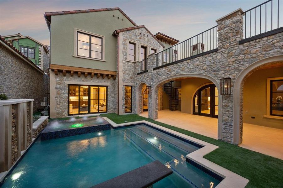 Courtyard at dusk featuring a balcony, stone siding, and a patio Courtyard at dusk featuring a balcony, stone siding, and a patio