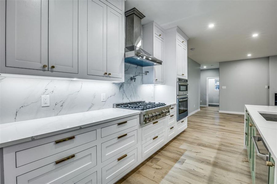 Kitchen featuring white cabinets, light hardwood / wood-style floors, wall chimney range hood, and appliances with stainless steel finishes