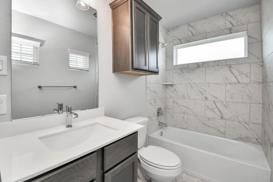 Secondary bath features tile flooring, bath/shower combo with tile surround, light stained wood cabinets, beautiful light countertop. Sample photo of completed home with similar floor plan. Actual colors and selections may vary.