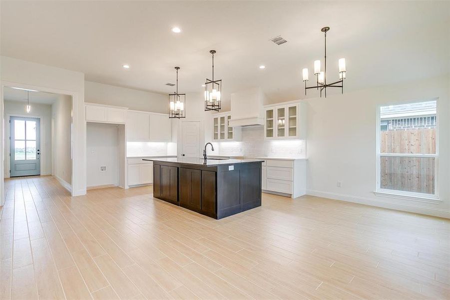 Kitchen featuring tasteful backsplash, a kitchen island with sink, light wood-type flooring, and white cabinetry