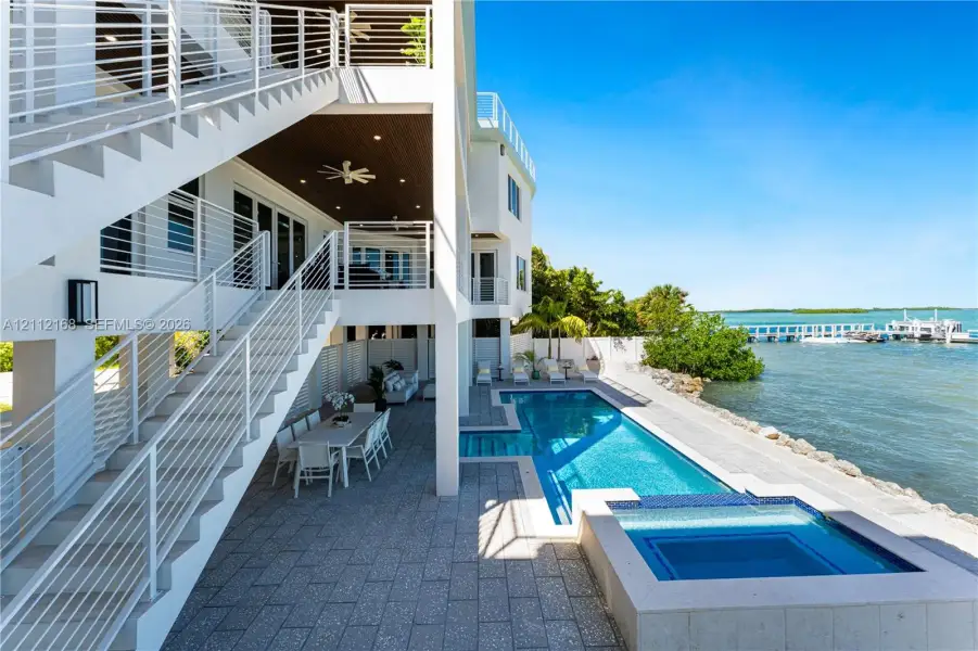 Multi-level exterior featuring a private swimming pool with integrated spa, paved pool deck, metal stair railings, and direct water access with a private dock Multi-level exterior featuring a private swimming pool with integrated spa, paved pool deck, metal stair railings, and direct water access with a private dock