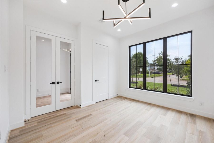Framed glass doors open into a light-filled office, where bold lighting and wide-plank floors elevate the space. Oversized windows provide a direct view of the front yard and neighborhood, creating an energizing setting for focus and creativity. Framed glass doors open into a light-filled office, where bold lighting and wide-plank floors elevate the space. Oversized windows provide a direct view of the front yard and neighborhood, creating an energizing setting for focus and creativity.