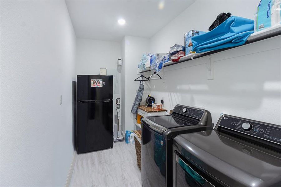 Dedicated laundry room featuring light wood-finish flooring, recessed lighting, and wall-mounted shelving