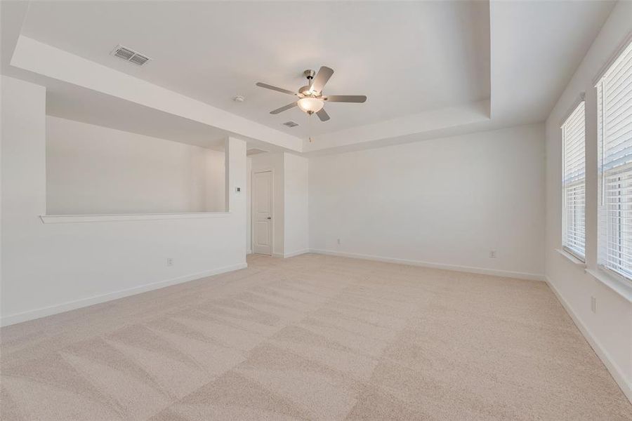 Carpeted empty room featuring a raised ceiling and ceiling fan