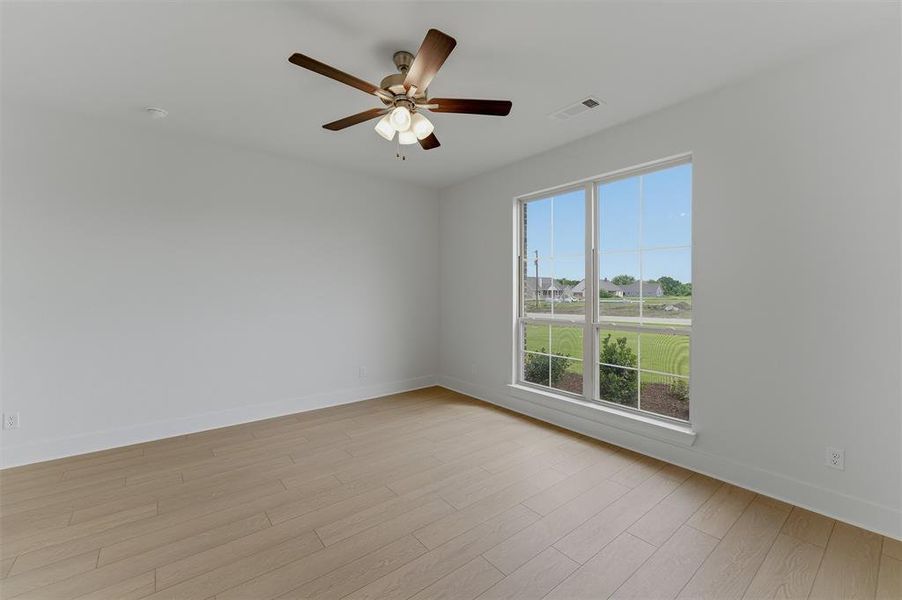 Spacious room featuring wood-finish flooring, a large window, white walls, and a ceiling fan with integrated lighting Spacious room featuring wood-finish flooring, a large window, white walls, and a ceiling fan with integrated lighting