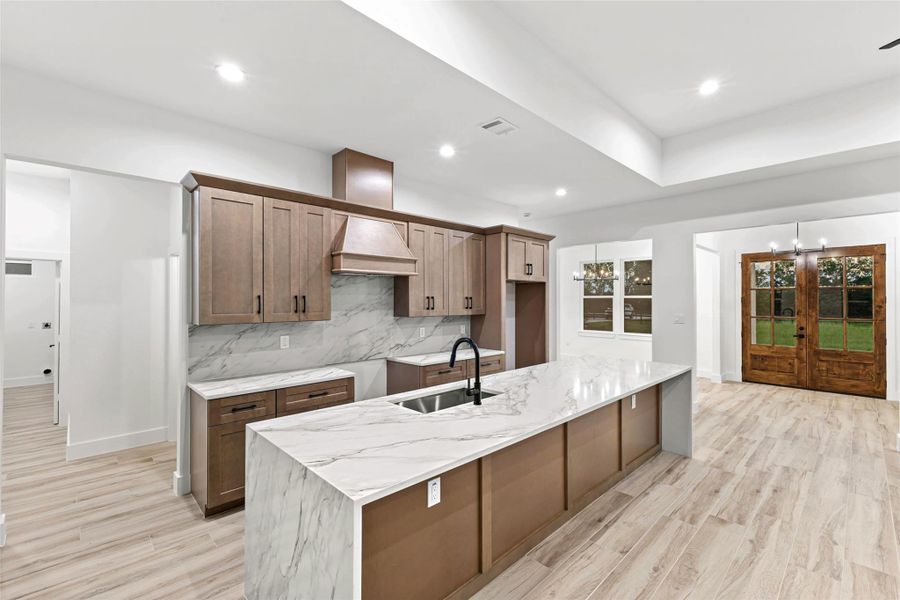 This modern kitchen features elegant quartz countertops, a spacious island with a sleek black faucet, and warm wooden cabinetry. The open layout seamlessly connects to a dining area with large windows and double glass doors, offering ample natural light and a welcoming atmosphere. This modern kitchen features elegant quartz countertops, a spacious island with a sleek black faucet, and warm wooden cabinetry. The open layout seamlessly connects to a dining area with large windows and double glass doors, offering ample natural light and a welcoming atmosphere.
