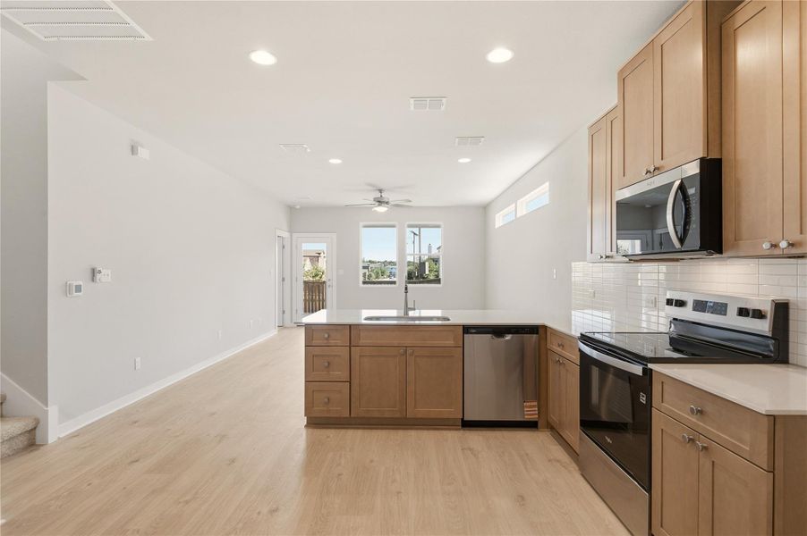 Kitchen featuring stainless steel appliances, a peninsula, backsplash, recessed lighting, and light wood-style flooring