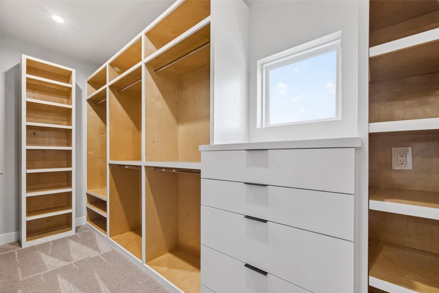 The primary suite's walk-in closet is outfitted with a custom built-in system featuring hanging rails, open shelving, and a built-in drawer unit, all in a warm wood-and-white finish. A window provides natural light, making this a bright and organized personal space.
