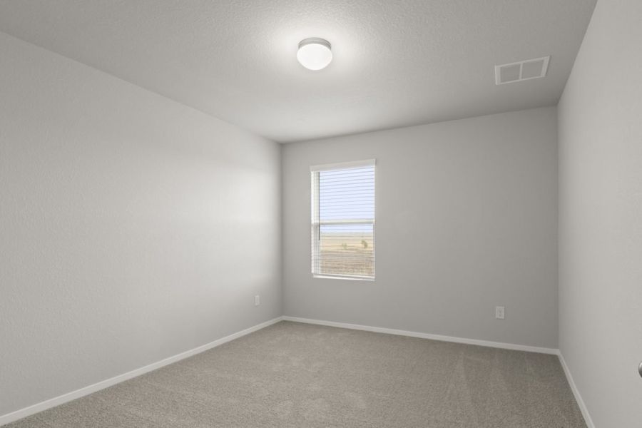 Image of a bedroom with tan carpeting and light grey walls with a window