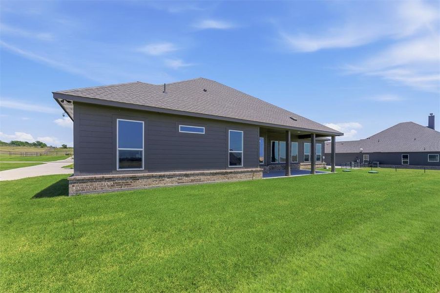 Spacious rear exterior featuring gray siding, a covered patio, a brick foundation, large windows, and a generously sized lawn area