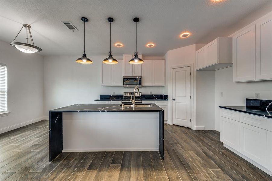 Kitchen with an island with sink, white cabinetry, decorative light fixtures, dark wood finished floors, and recessed lighting Kitchen with an island with sink, white cabinetry, decorative light fixtures, dark wood finished floors, and recessed lighting