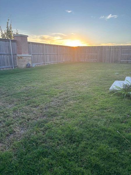 Expansive grassy yard with a wooden privacy fence, featuring a decorative stone and brick pillar