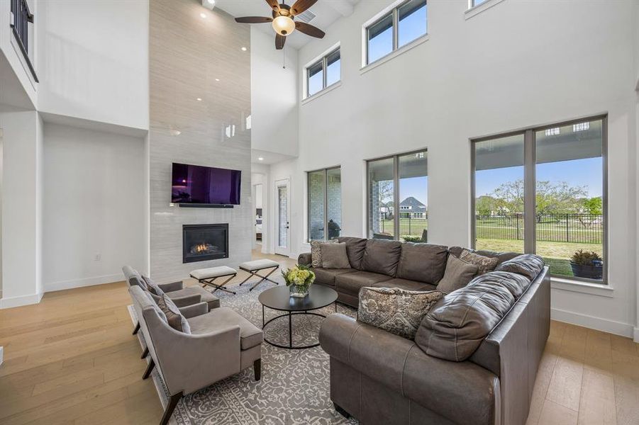 Living area featuring a fireplace, light wood finished floors, ceiling fan, and a high ceiling