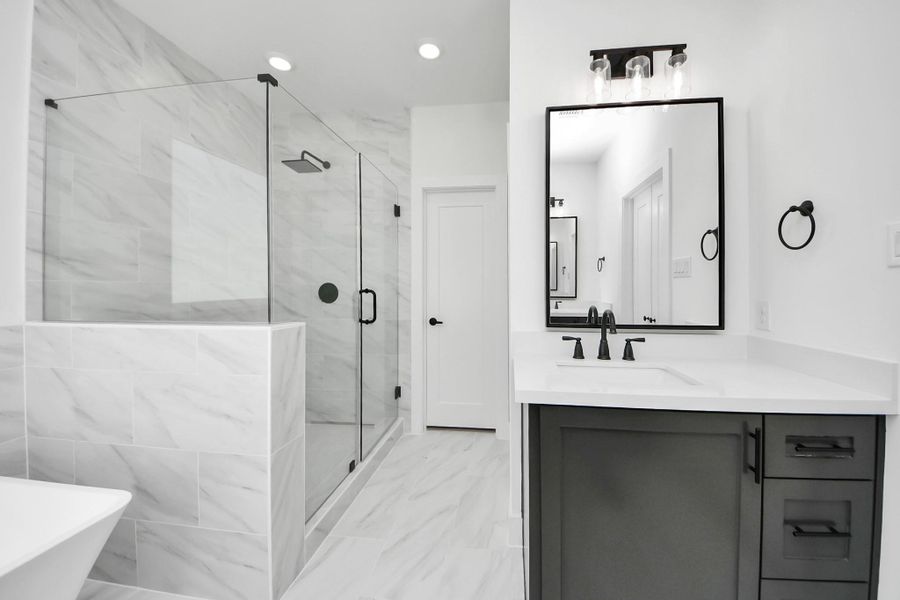 This bathroom features a modern design with a spacious glass-enclosed shower, large wall tiles, and a sleek vanity with a black-framed mirror. The neutral color palette and stylish fixtures create a clean, contemporary look.