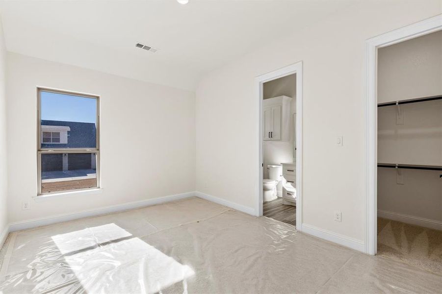 Guest bedroom featuring a walk in closet, carpet,  closet, vaulted ceiling, and connected bathroom