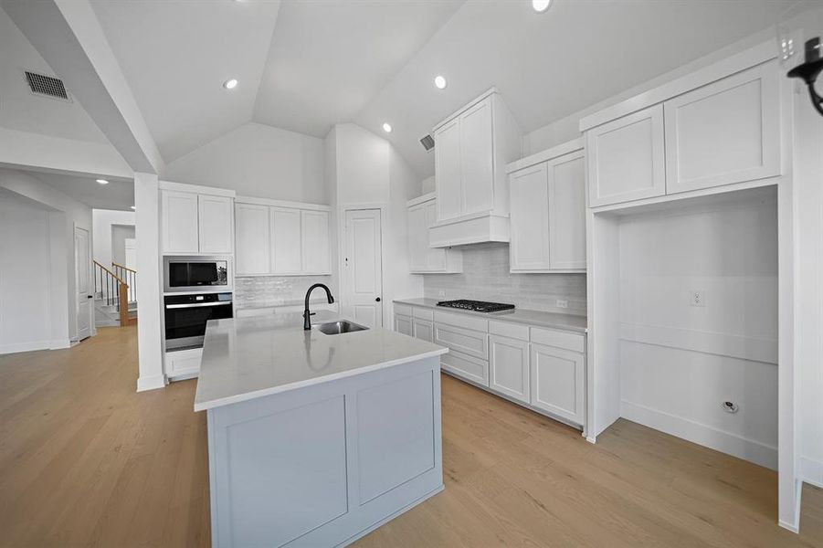Kitchen with white cabinetry, backsplash, lofted ceiling, light wood-style flooring, and appliances with stainless steel finishes