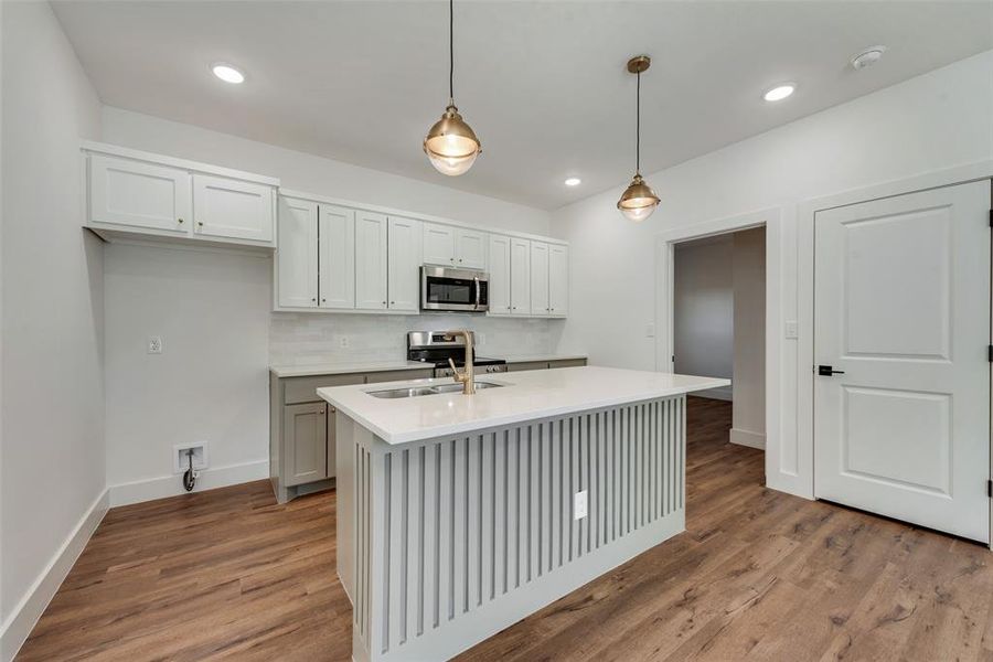 Kitchen featuring pendant lighting, backsplash, appliances with stainless steel finishes, white cabinets, and light wood-type flooring Kitchen featuring pendant lighting, backsplash, appliances with stainless steel finishes, white cabinets, and light wood-type flooring