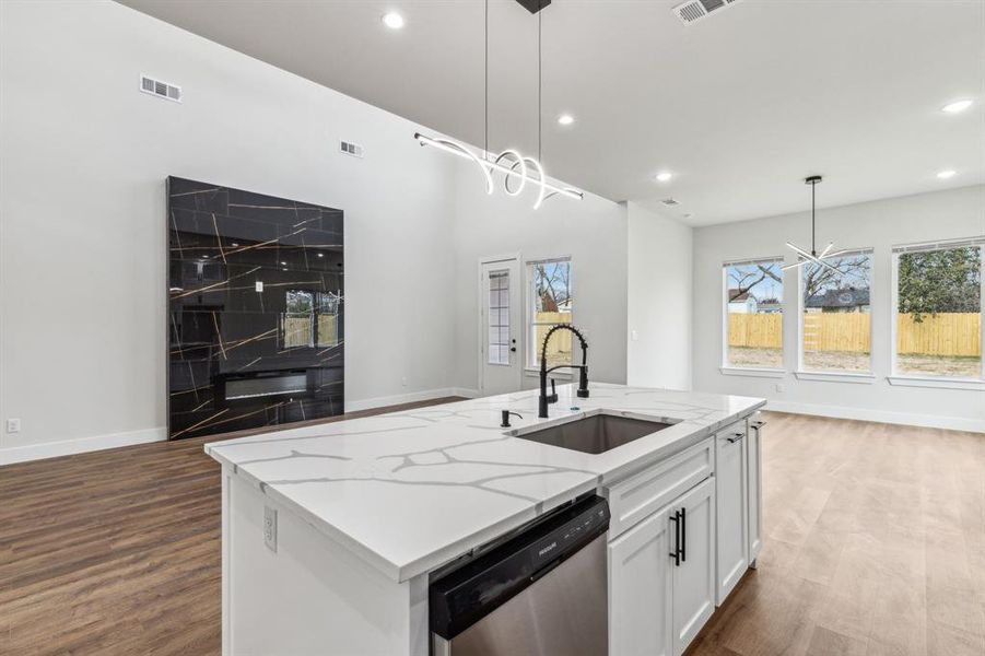 Kitchen with white cabinetry, a center island with sink, dishwasher, pendant lighting, and sink