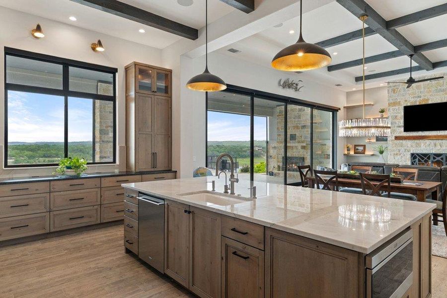 Open-concept kitchen featuring an oversized island with an integrated sink and built-in appliances, light wood-finish cabinetry, a coordinated stone countertop, and wood-finish flooring