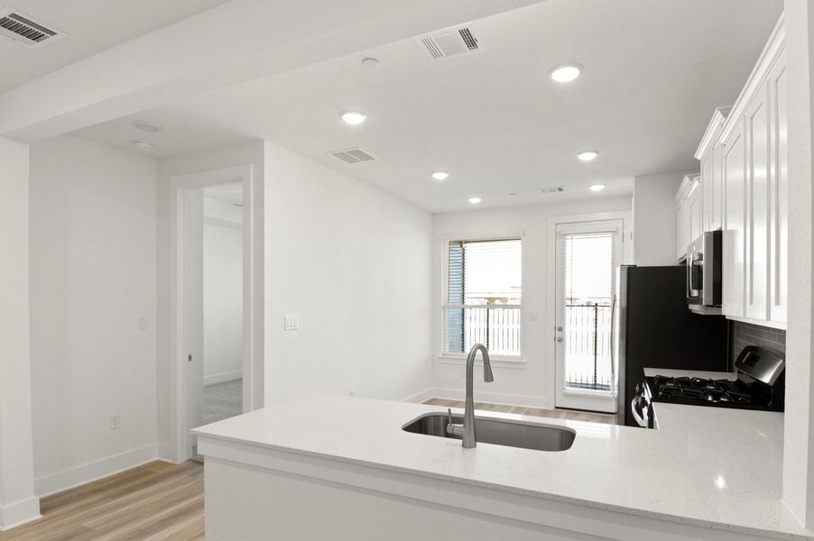 Kitchen featuring a peninsula, light stone counters, white cabinetry, stainless steel appliances, and light wood-style floors