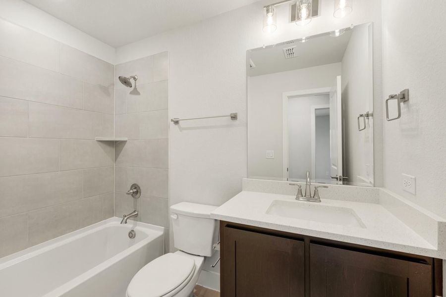 Bathroom with tiled tub and shower, dark wood vanity, white quartz countertop, and large mirror