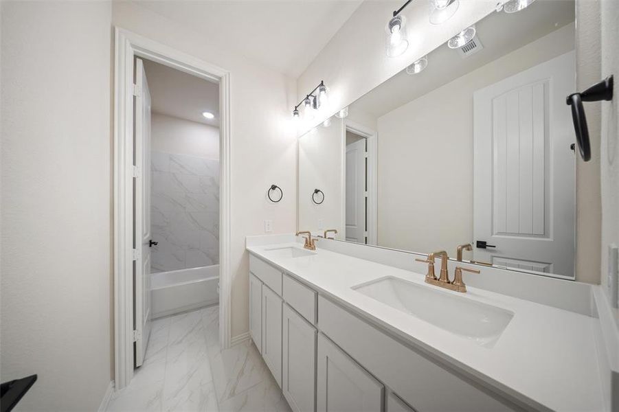 Full bathroom with double vanity, light marble finish floors, and bathtub / shower combination