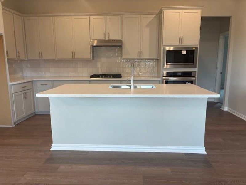 Kitchen featuring stainless steel appliances, dark wood-style floors, decorative backsplash, and a center island with sink Kitchen featuring stainless steel appliances, dark wood-style floors, decorative backsplash, and a center island with sink
